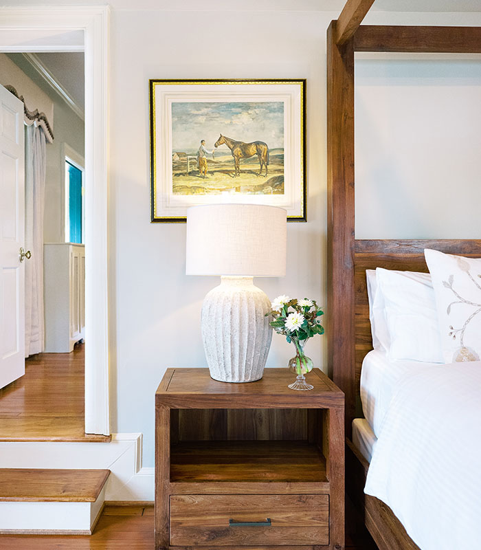 Cozy bedroom with a wooden nightstand, a lamp, and a painting of a horse on the wall