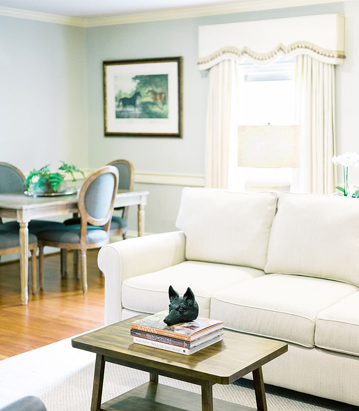 Elegant living room with a white couch, coffee table, and dining area in the background