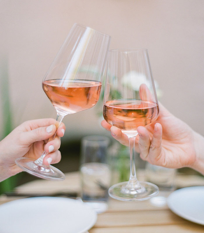 Two people toasting with glasses of rosé wine at an outdoor dining table